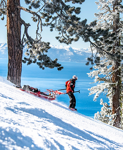 female patroller pulls toboggan down slope with Lake Tahoe views